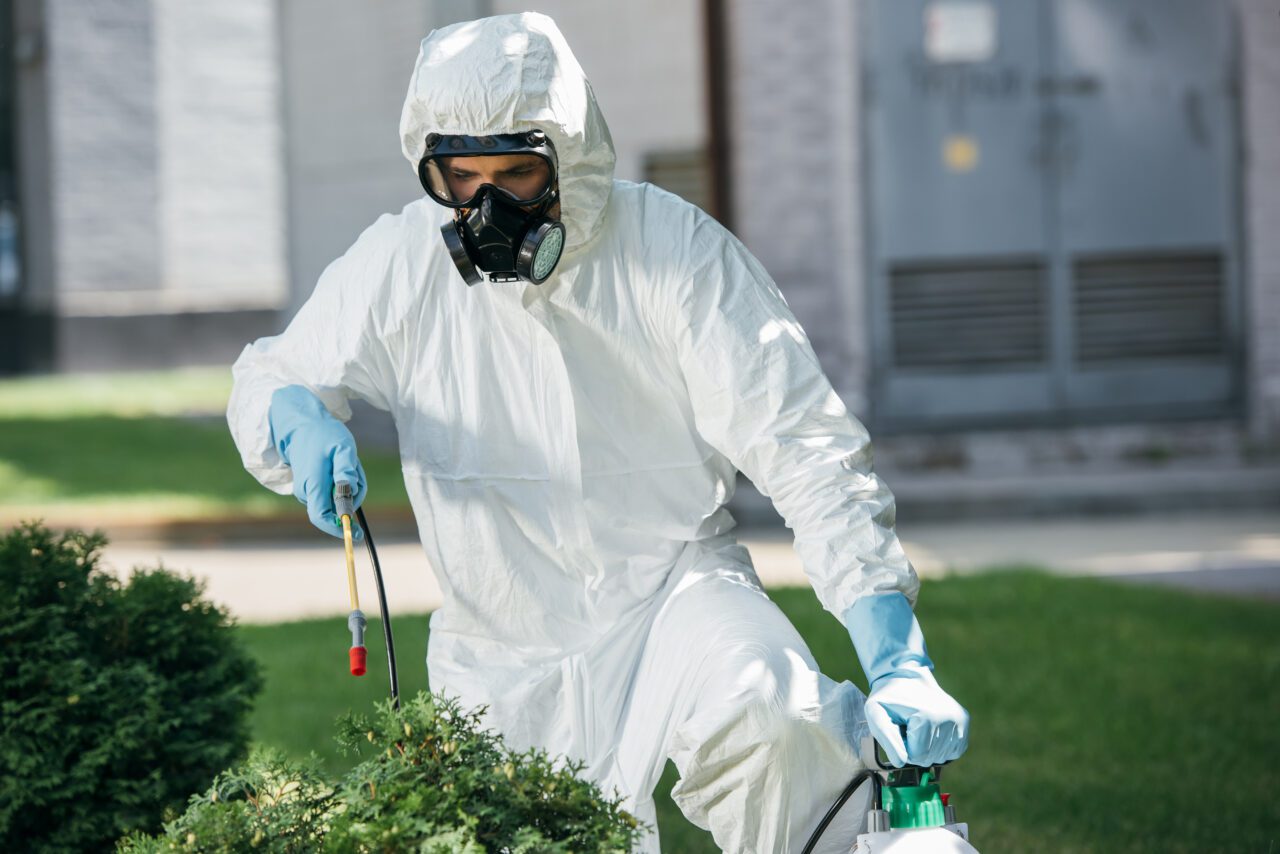 male pest control worker in uniform spraying chemicals on bush e1697926892145